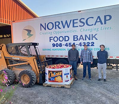 Three men standing in front of a truck that says 'NORWESCAP FOOD BANK' on it.