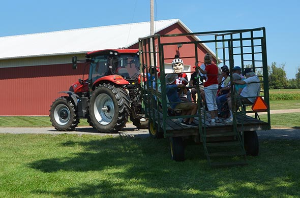 Scarlet Knight and passengers on wagon being pulled by red tractor.